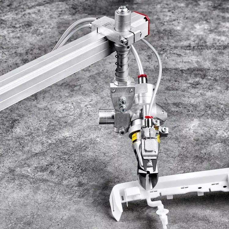 Pneumatic gripper attached to a robotic arm holding a white plastic part on a stone floor