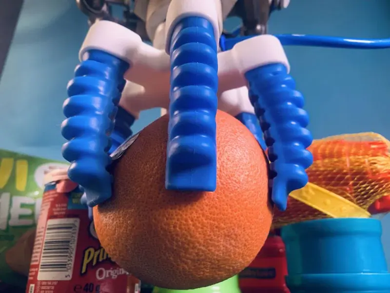 front view of a three finger centric gripper holding an orange
