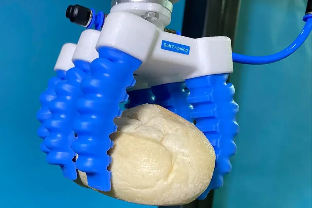 Blue SoftGripping soft gripper with four fingers holding a bread roll