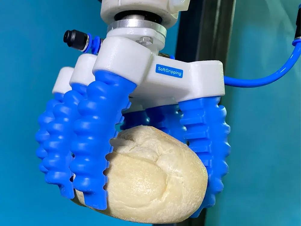 SoftGripping Soft Gripper with three blue fingers gripping a piece of bread