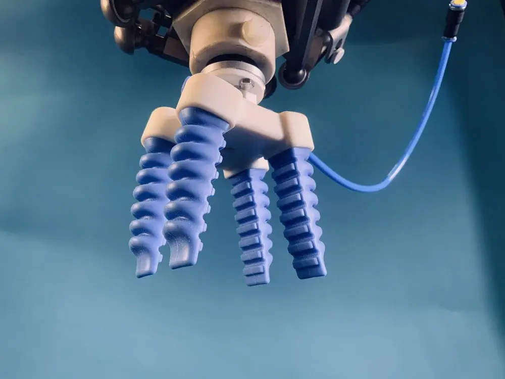 Soft gripper with four blue fingers attached to a robotic arm, blue background