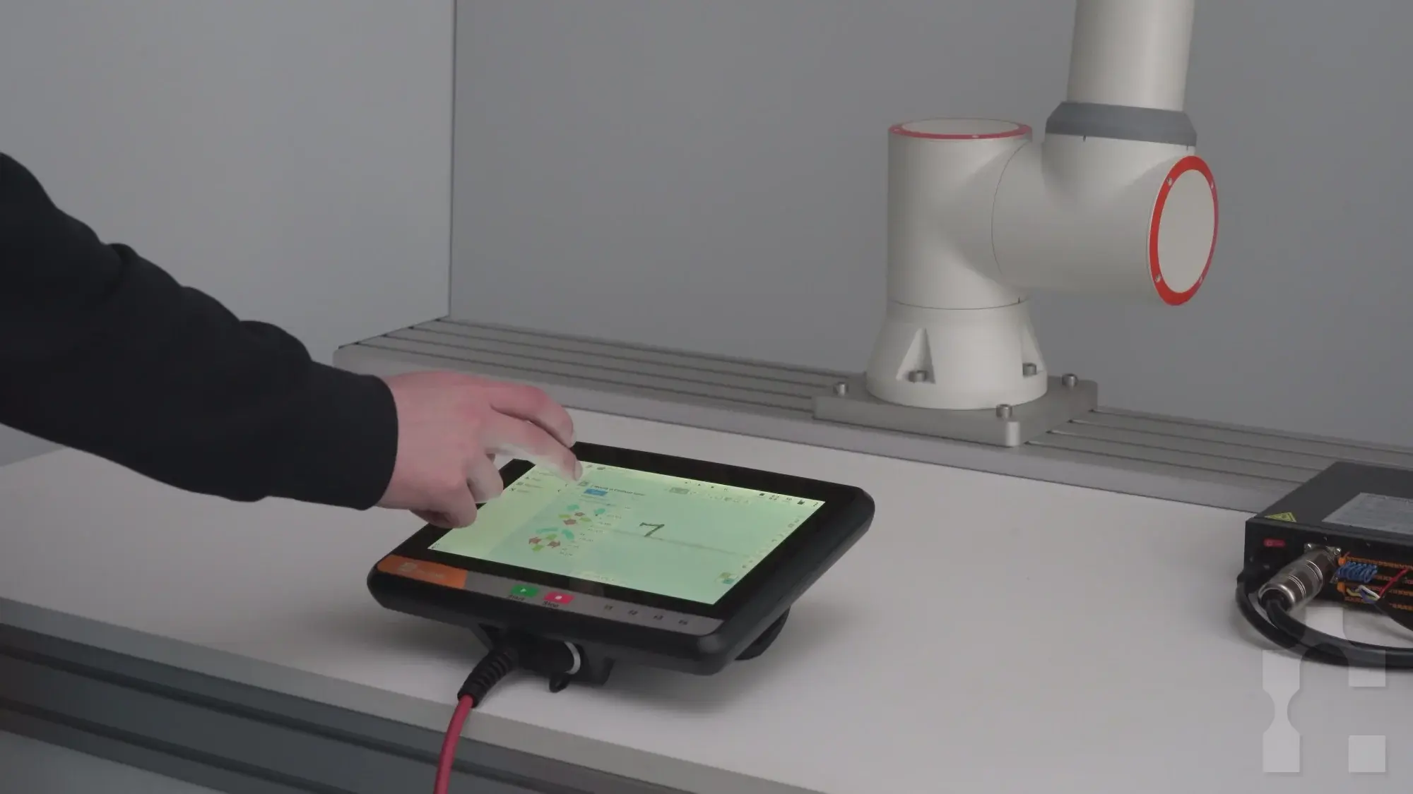 Hand operating a Fairino Teach Pendant on a table next to a robot arm