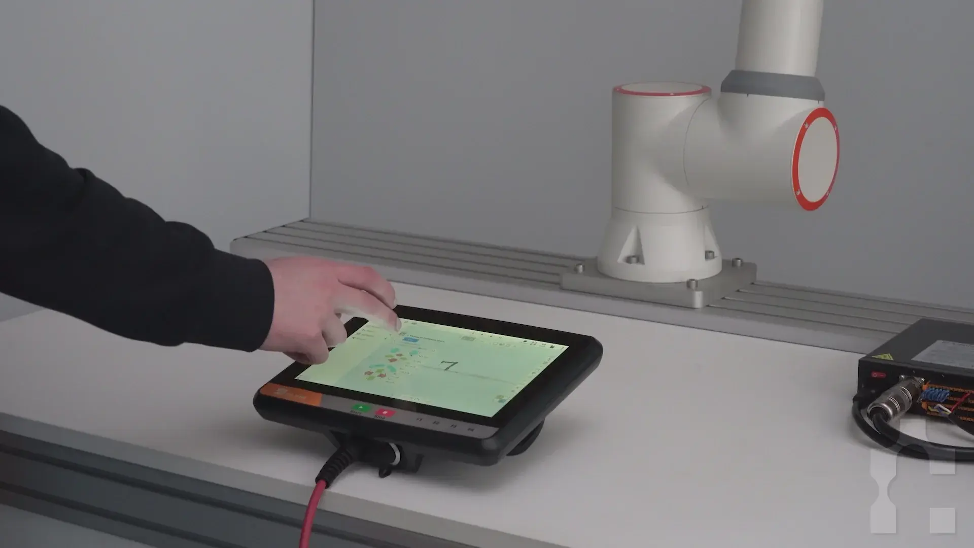 Side view of Fairino teach pendant with hand interacting, connected to a device beside a robot arm