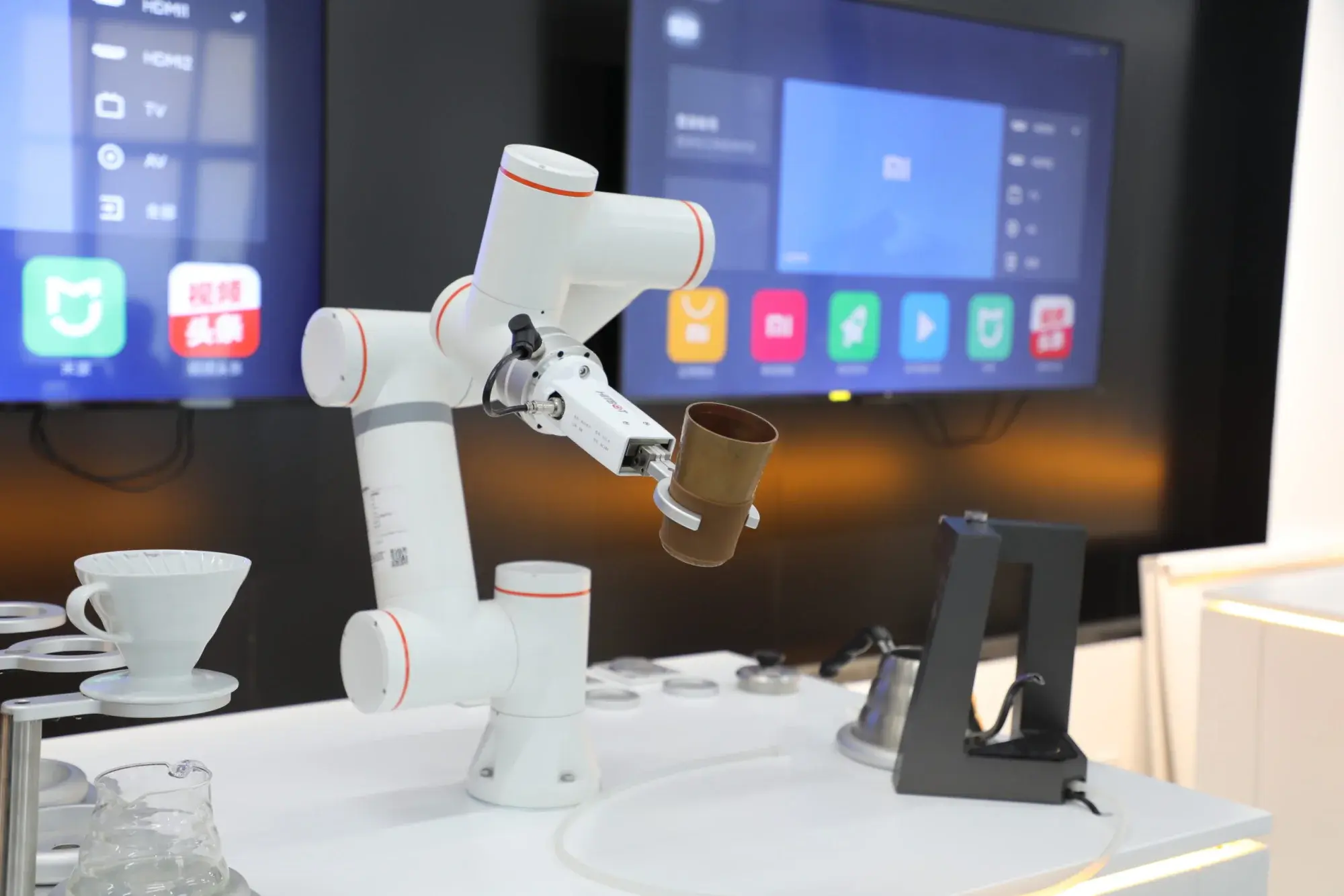 White industrial robotic arm operating in a kitchen setup holding a brown cup